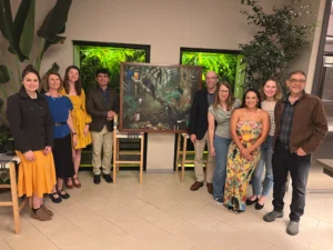 A group of fellows smile for the camera circled around a painting.